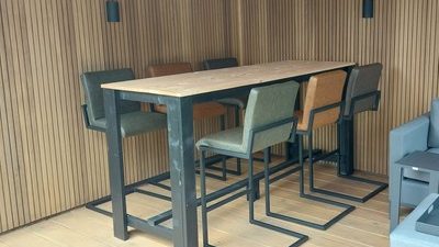 Bartafel steigerhout met zwarte poten Een lange steigerhouten bartafel met vijf stoelen in een moderne, houten overkapping.