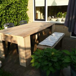 Tuintafel en bank steigerhout Steigerhouten tafel met bank in een buitenruimte, omringd door groene planten.