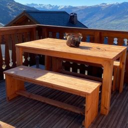 Tuinset douglas steigerhout Houten tafel en bank op een balkon met uitzicht op bergen en een blauwe lucht.